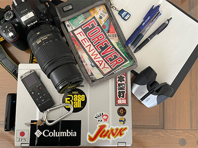 記者の七つの道具「カメラ、ボイスレコーダー、取材ノート、3種類のペン、双眼鏡、パソコン、取材パスホルダー兼ペン入れ」。取材パスホルダーには神奈川大学のキーホルダーが付いている。